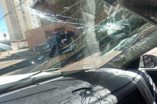 No alto do vidro, o furo causado por um dos tiros que acertaram o homem em fuga; ao fundo, viatura da GM preserva o local