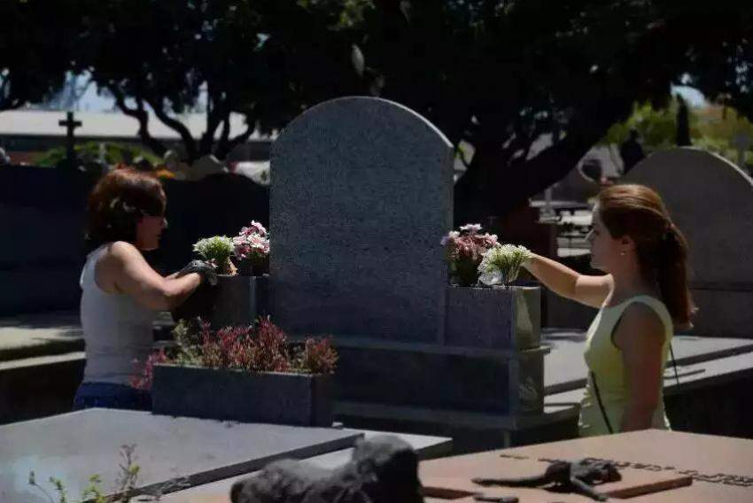 Mulheres próximas à lápide em cemitério