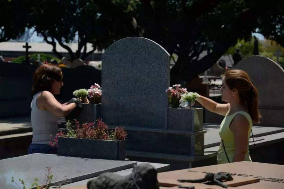 Mulheres próximas a lápide em cemitério