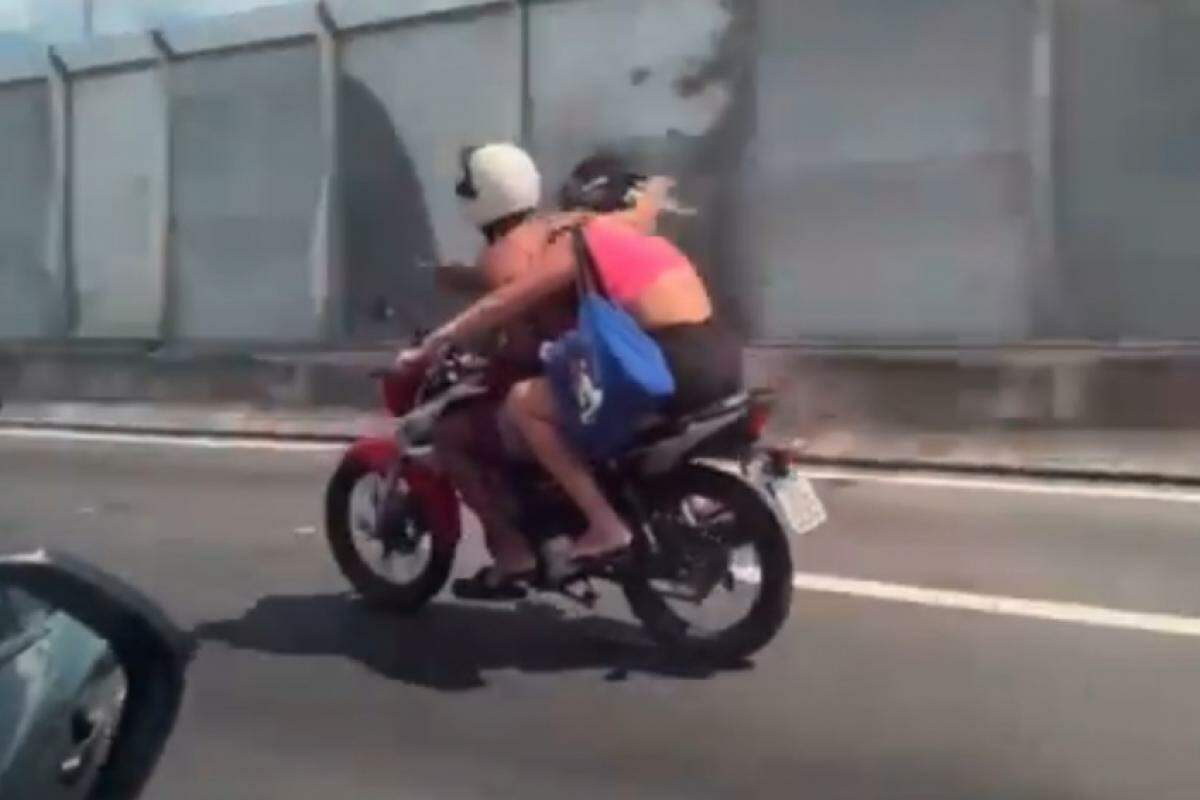 Motoqueiro come marmita enquanto garupa pilota a moto