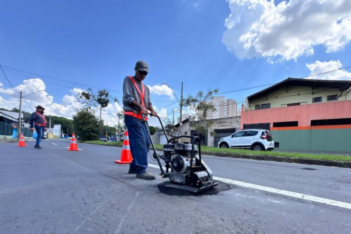 Para facilitar a cobertura de aberturas de pequeno diâmetro no asfalto, equipe utiliza placa vibratória e massa fria