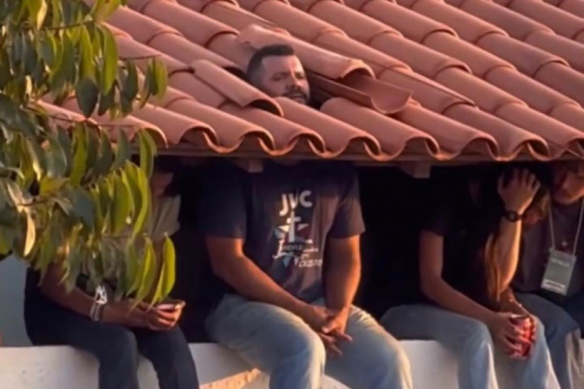 Fã com a cabeça em meio as telhas para acompanhar show de Frei Gilson 