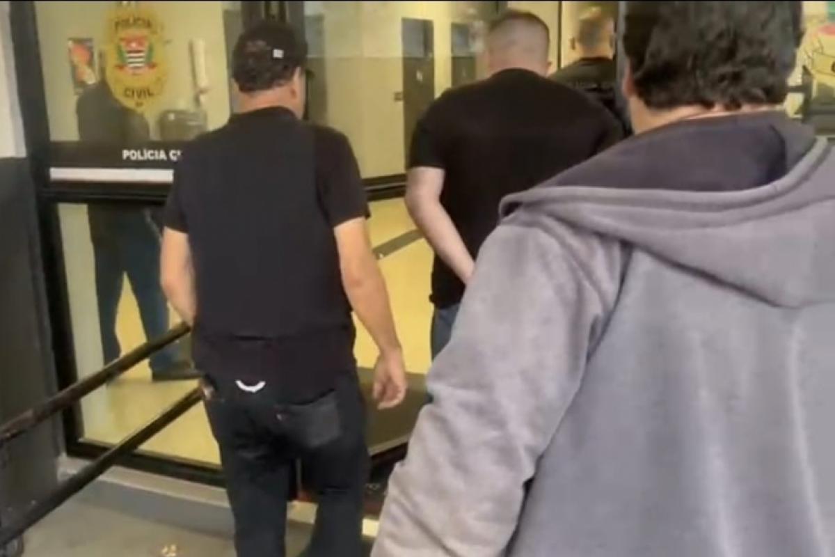 Investigado sendo conduzido por policial na delegacia