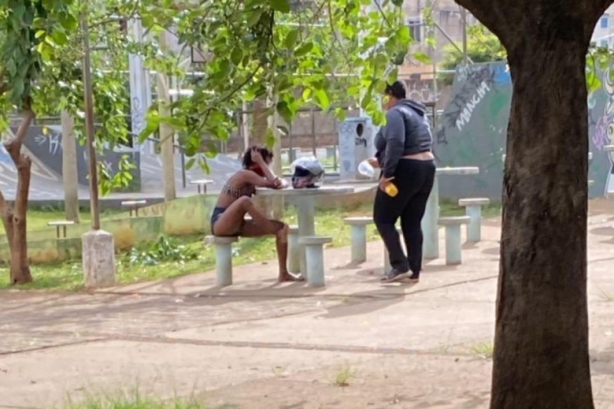 Vítima sentada na praça, após ser esfaqueada pelo companheiro, aguardando socorro